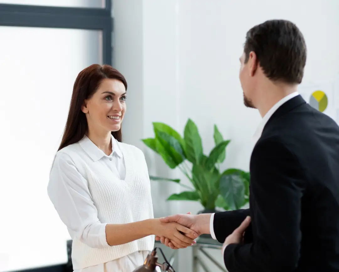 A professional setting with two individuals shaking hands, a desk with a coffee cup and papers, and greenery in the background A professional setting with two individuals shaking hands, a desk with a coffee cup and papers, and greenery in the background